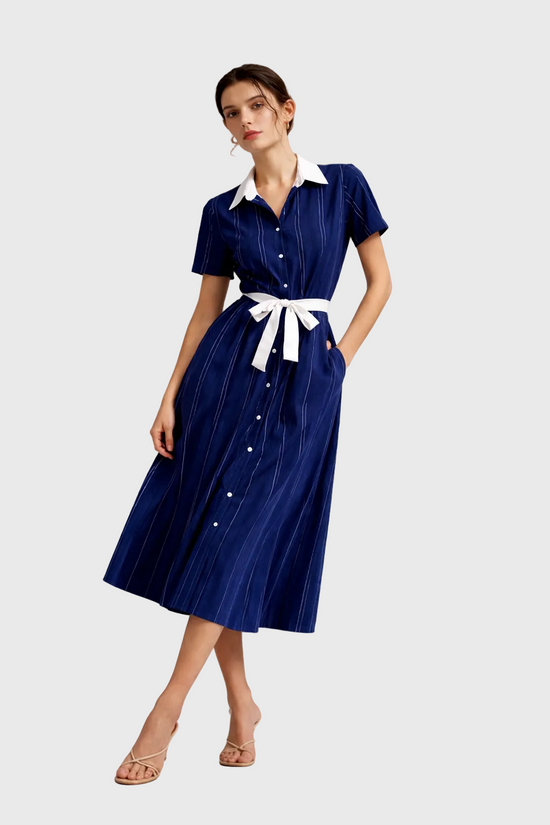 Woman wearing a blue dress with a white collar and belt on a gray background