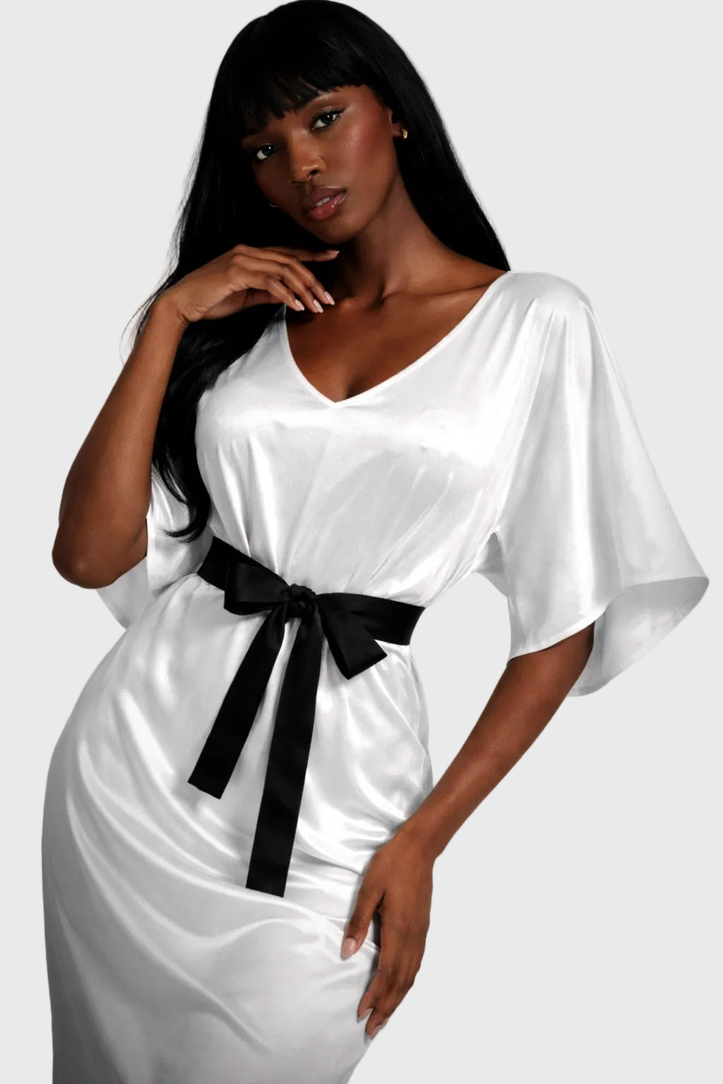 Woman wearing a white dress with a black belt against a gray background