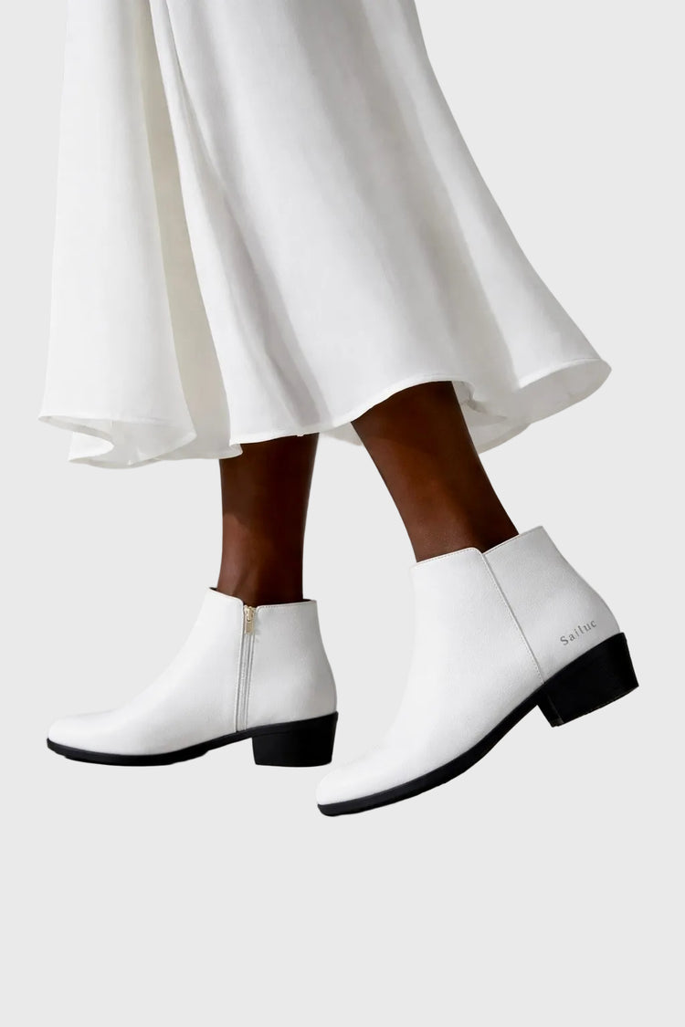 White ankle boots worn with a white skirt on a light gray background