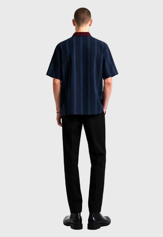 Man wearing a navy pinstripe shirt and black pants on a gray background