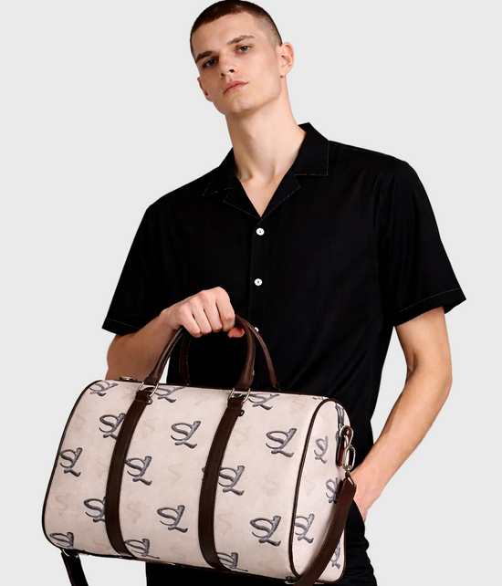 Man holding a light gray duffel bag with brown handles against a plain background