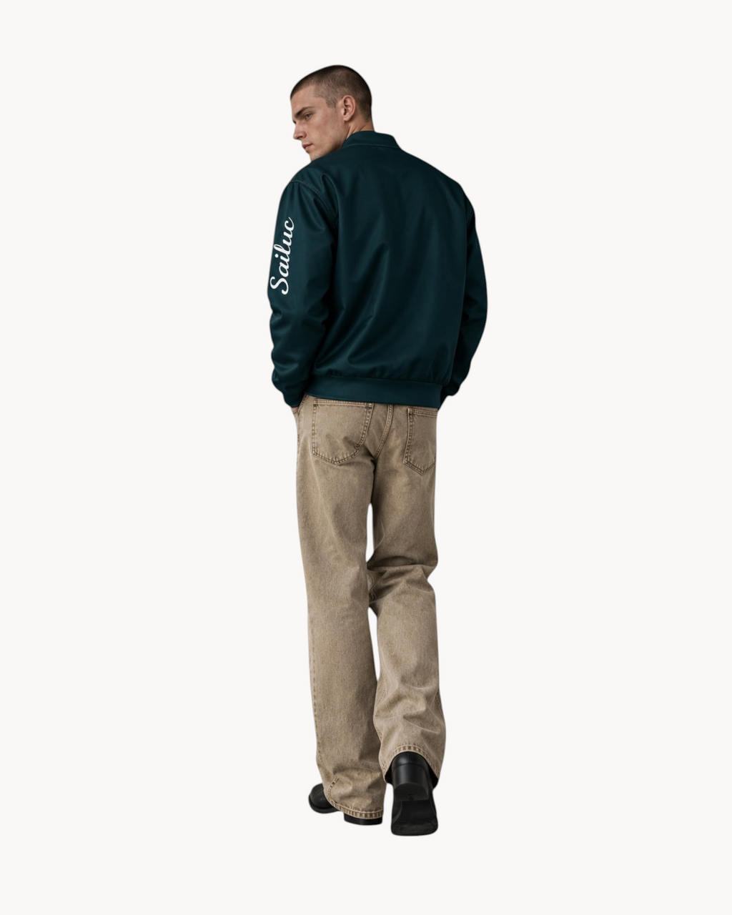 Model wearing a dark green Sailuc Vesper bomber jacket with a white logo on the sleeve and relaxed beige trousers.