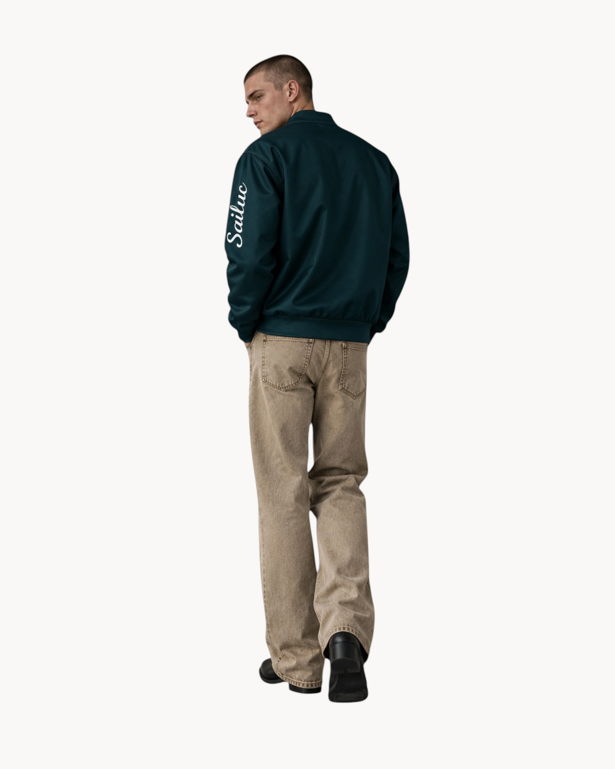 Model wearing a dark green Sailuc Vesper bomber jacket with a white logo on the sleeve and relaxed beige trousers.