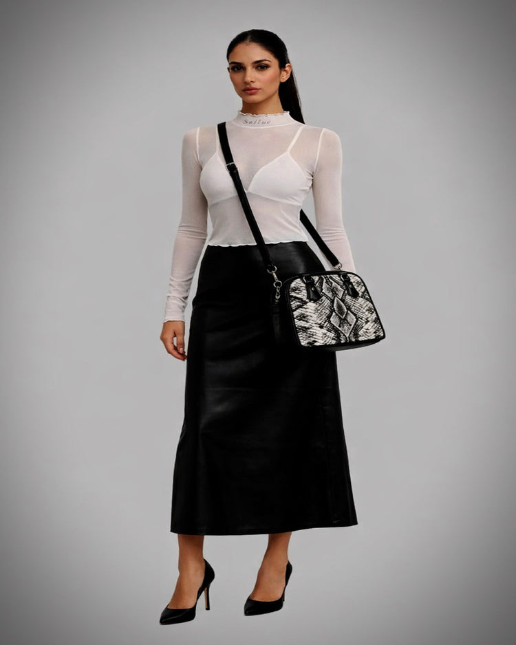 Woman wearing a black skirt and white top with a black and white patterned bag on a gray background