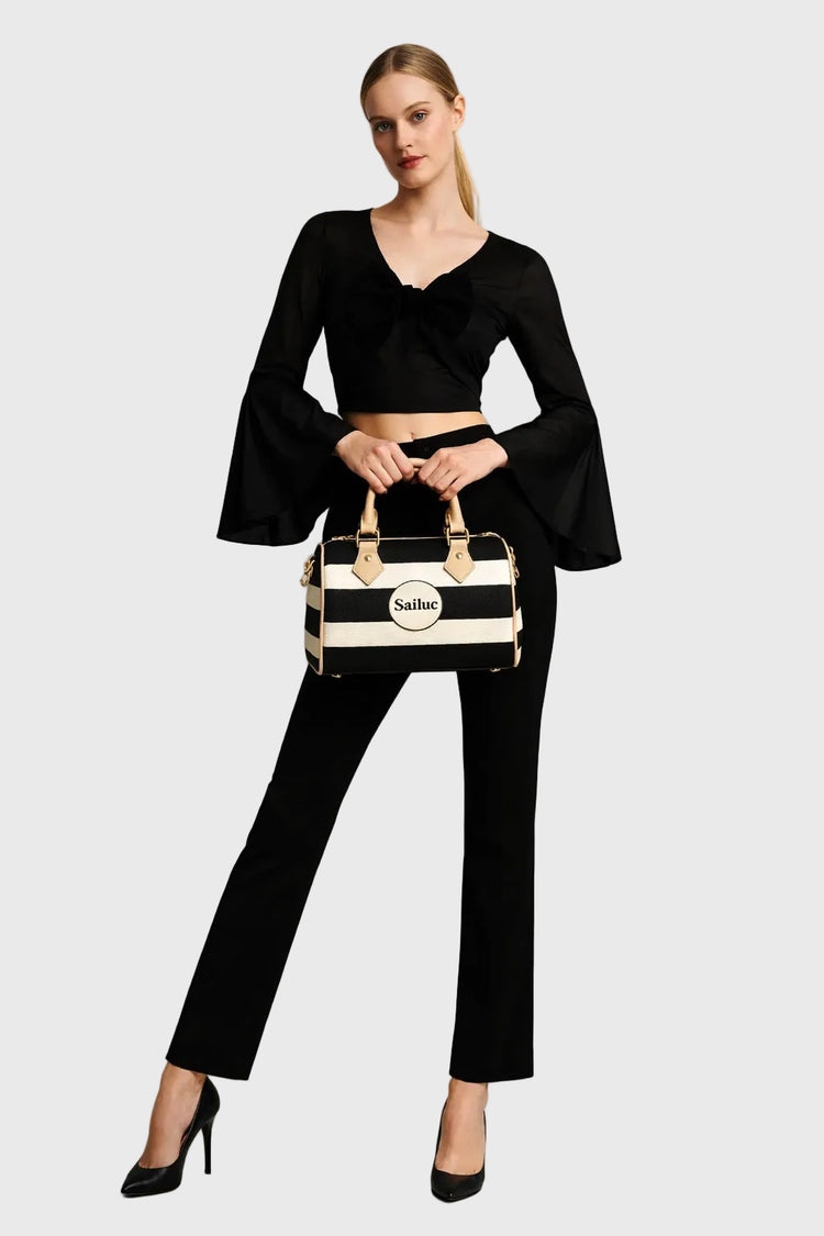 Woman in black outfit holding a striped handbag on a gray background