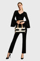Woman in black outfit holding a striped handbag on a gray background