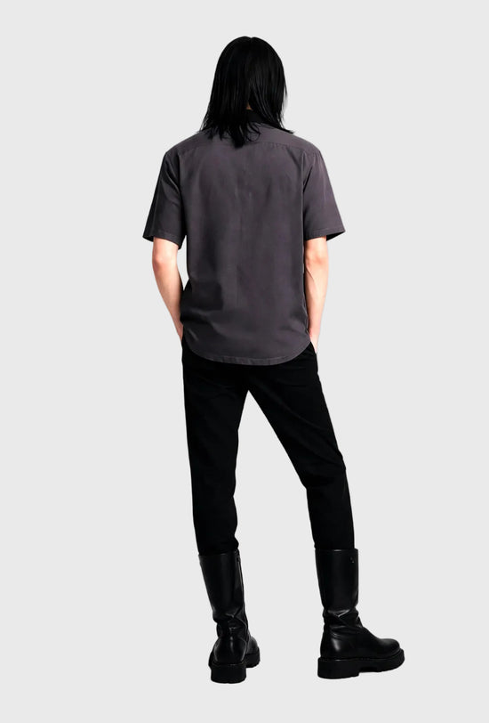 Person wearing a dark gray t-shirt and black pants standing against a plain background