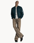 A man wearing a dark teal Sailuc Vesper bomber jacket with a silver zipper and white sleeve branding over a white tee.