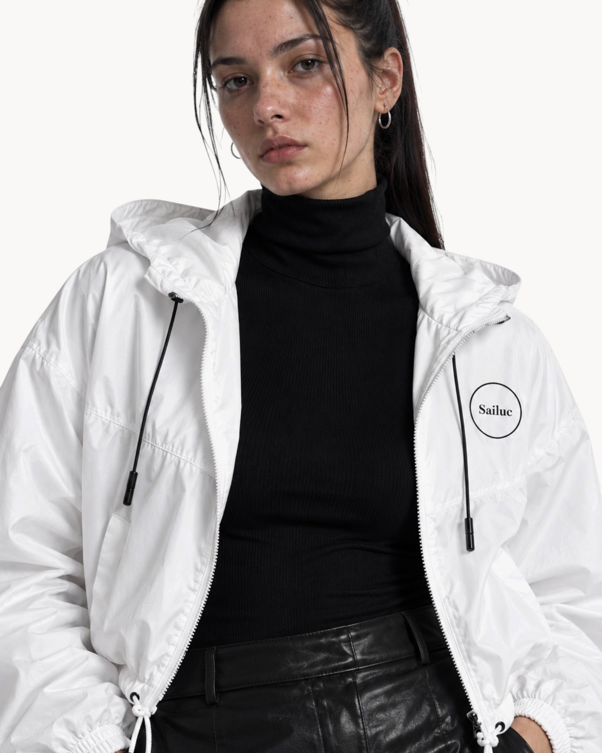 Model wearing a white Sailuc cropped windbreaker with a hood, half-zip, and adjustable drawcords over a black top.