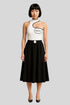 Woman in luxury Sailuc black skirt and white asymmetric top with logo, standing on gray background