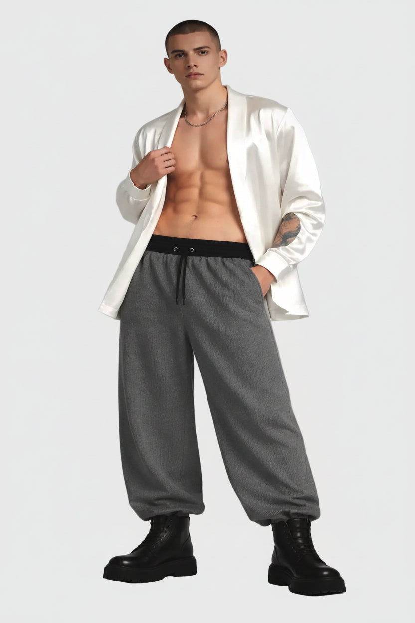 Man wearing a white silk cardigan, gray pants, and black boots on a gray background