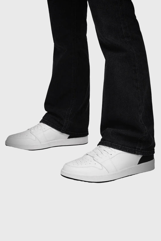 White sneakers worn with black jeans on a gray background