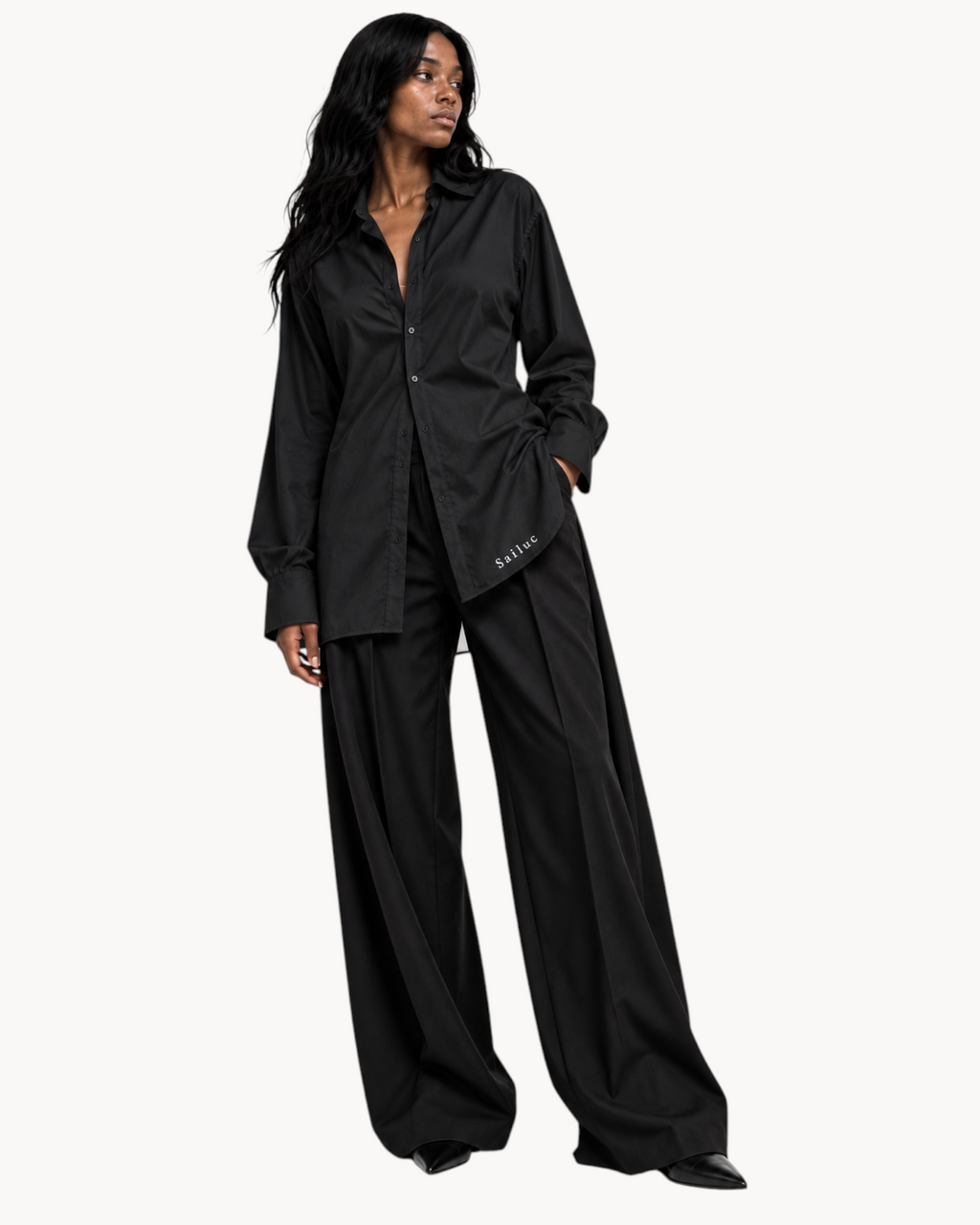 Model wearing a black Sailuc Linea longline shirt with a classic collar and wide-leg trousers against a white background