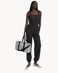 Model holding a white Sailuc Essential Voyage Bag with black monogram print, black handles, and black hardware.