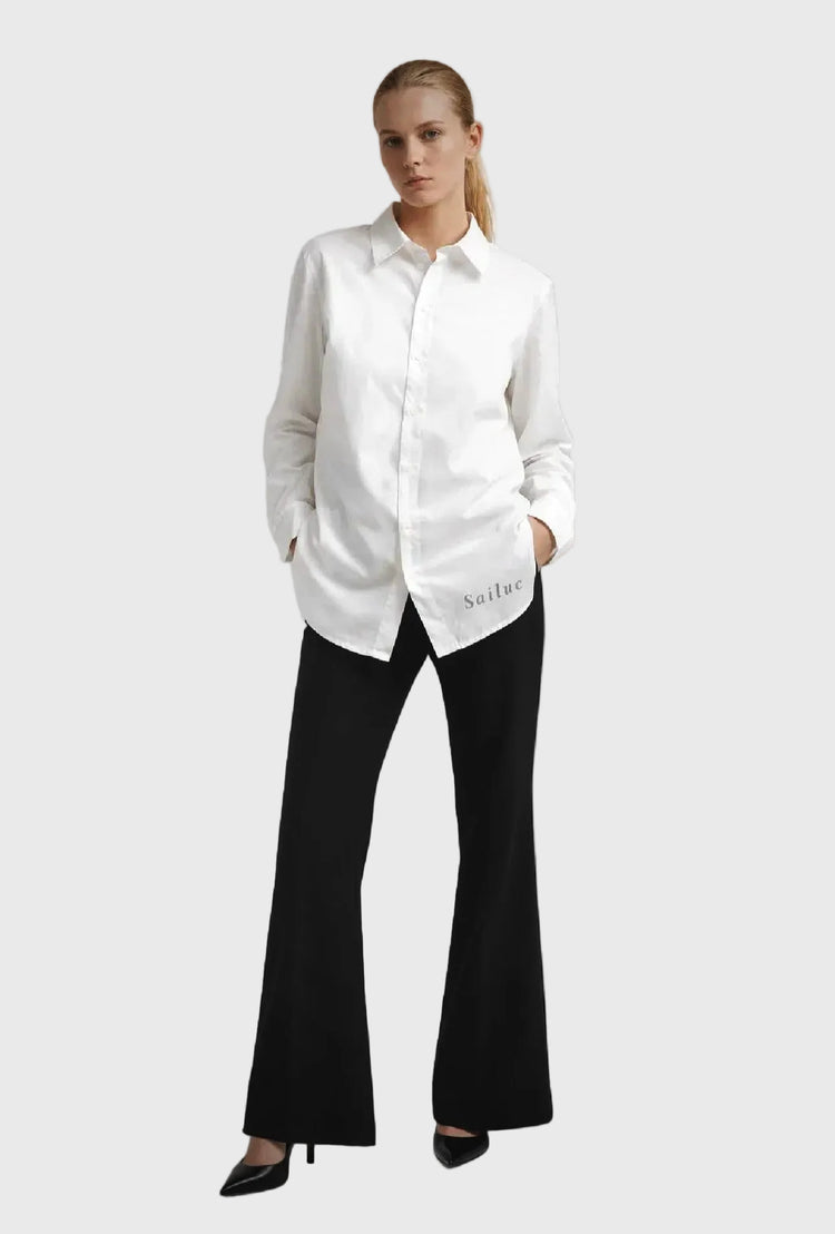 Woman wearing a long sleeve white shirt and black pants on a gray background