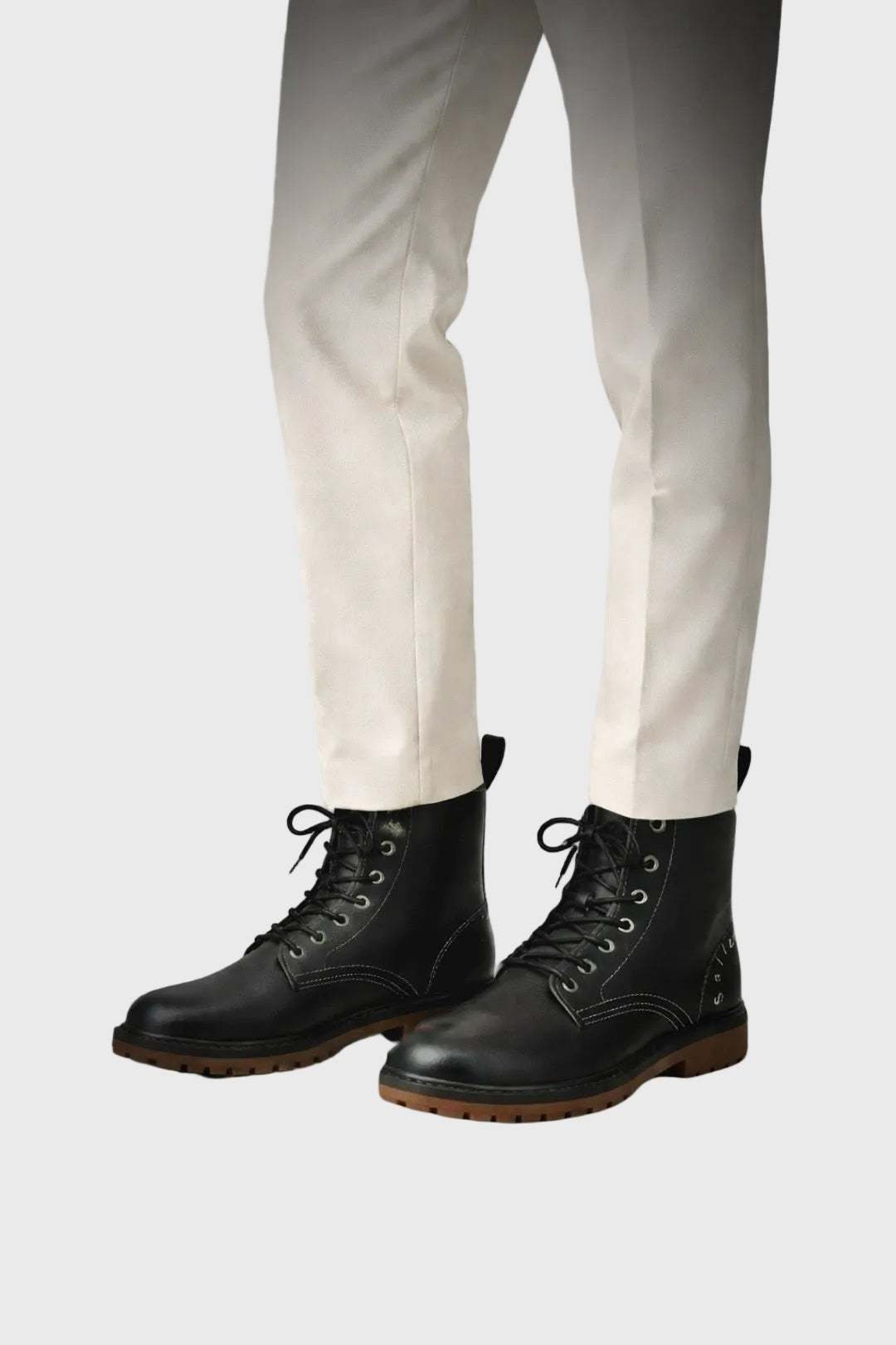 Black boots worn with white pants on a gray background
