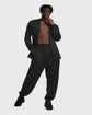 Man wearing a black cardigan over loose fitted trousers against a gray background