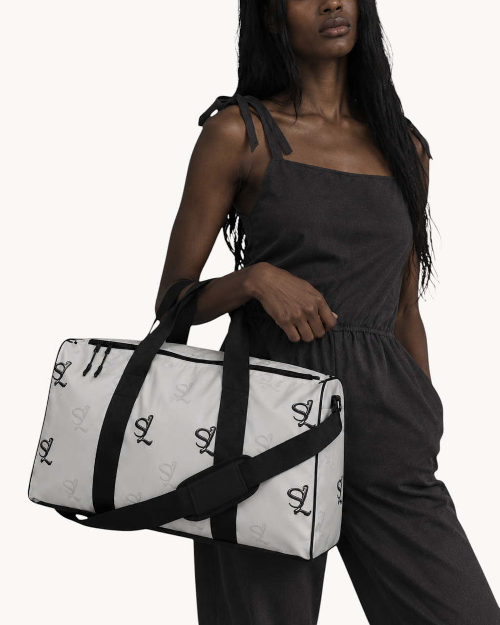 Model carrying a white Sailuc Essential Voyage Bag with black monogram print, carry handles, and shoulder strap.