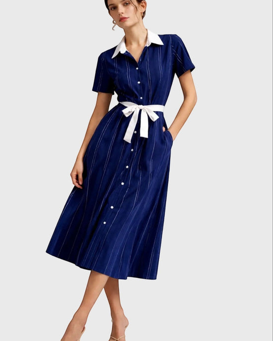 Woman wearing a blue dress with a white collar and belt on a gray background